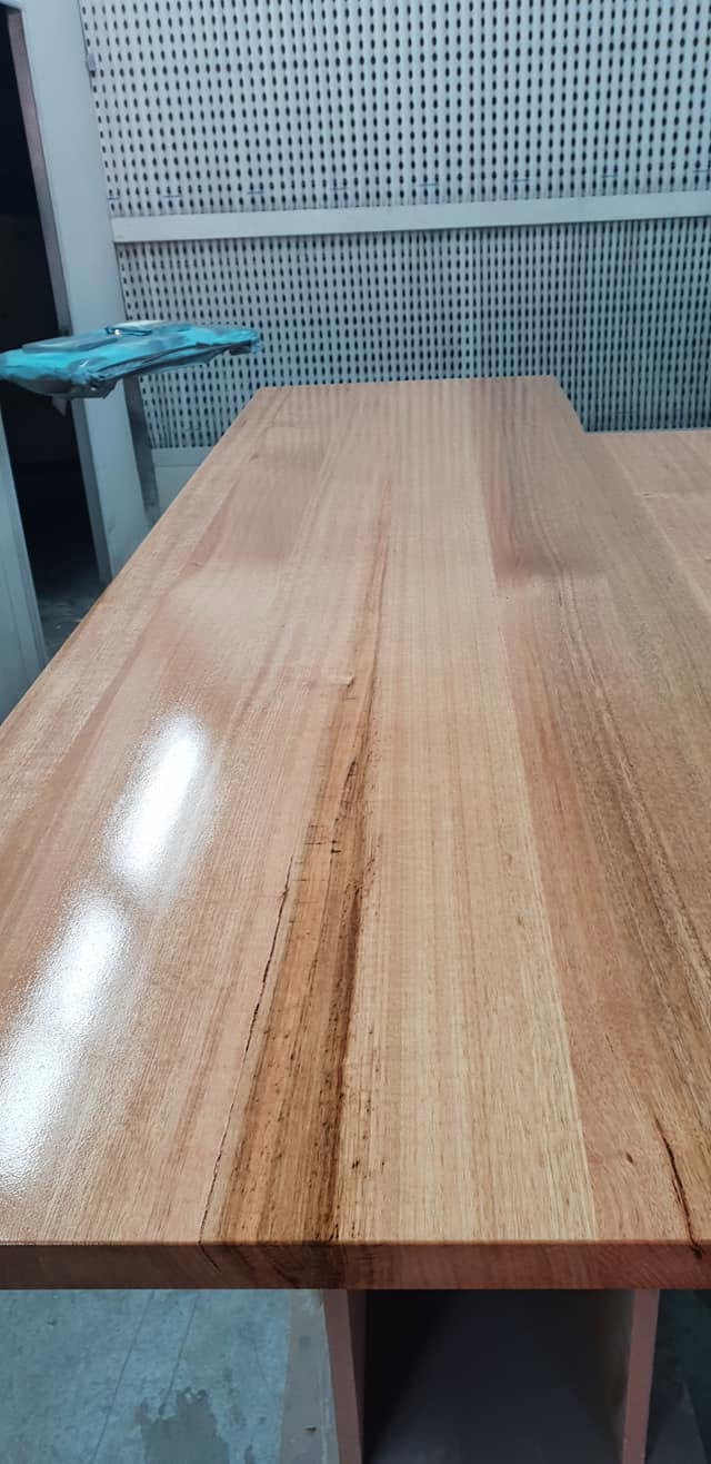 Long timber benchtop under a satin clear coat catching the workshop lights
