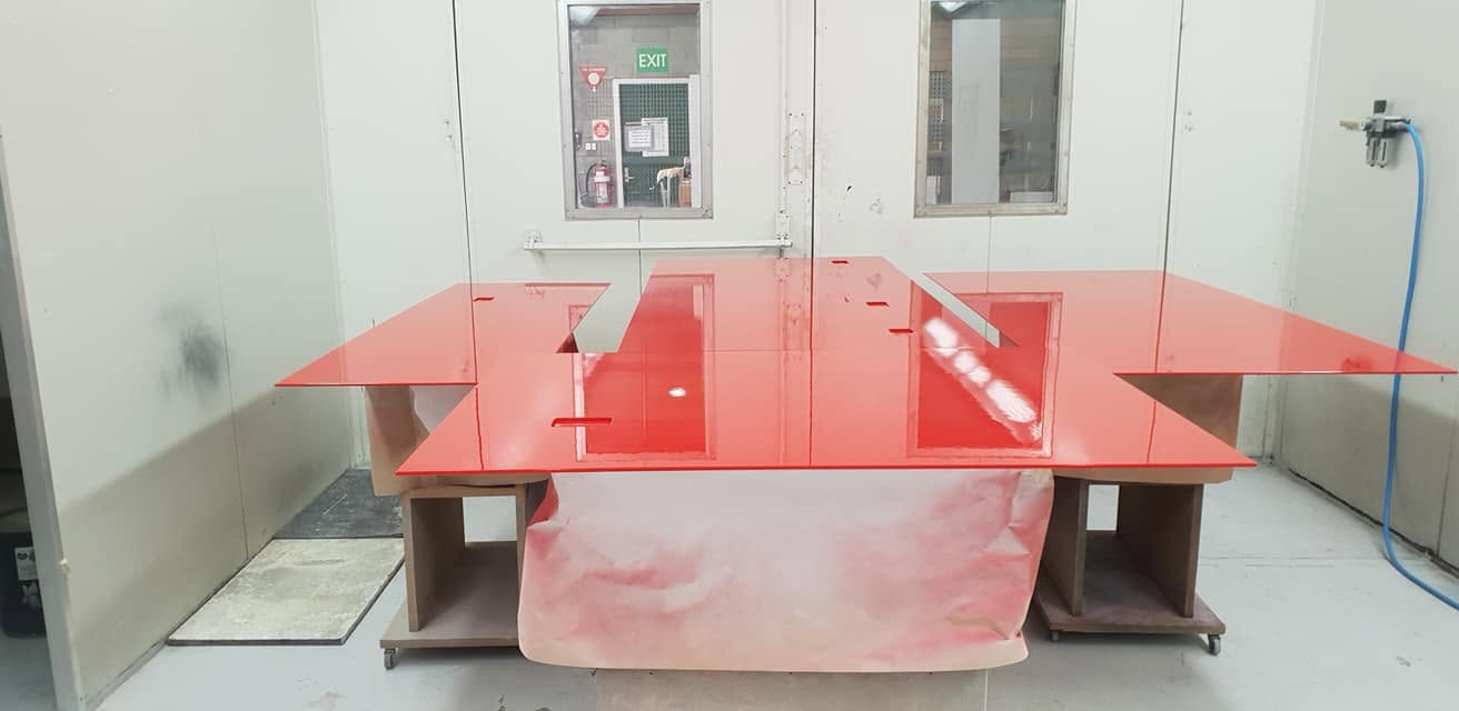 Red back-sprayed glass panel set up on trestles inside the controlled spray booth