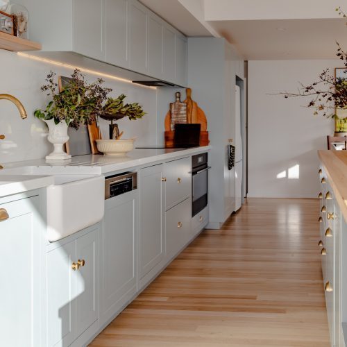 Spray painted shaker kitchen cabinetry in soft grey with brass handles in a Blackmans Bay home near Hobart